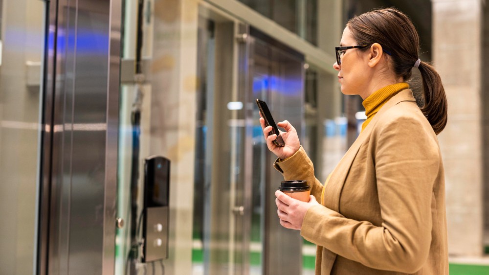devojka stoji ispred hotelskoh vrata sa telefonom u ruci